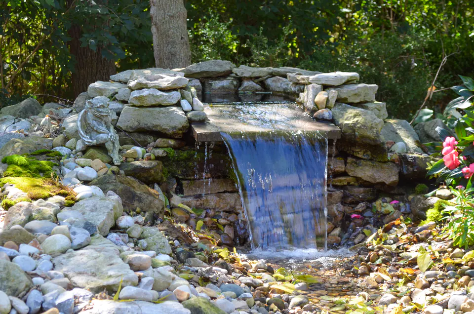 Natural stone waterfall dropping from a low wall into a planted garden basin